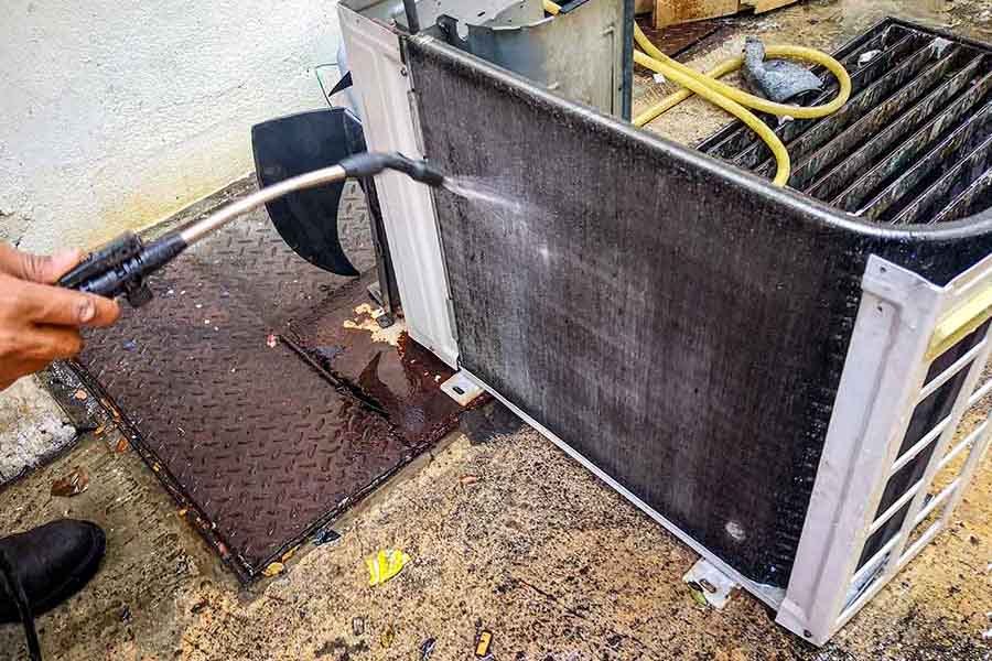 Technician pressure washing during AC coil cleaning